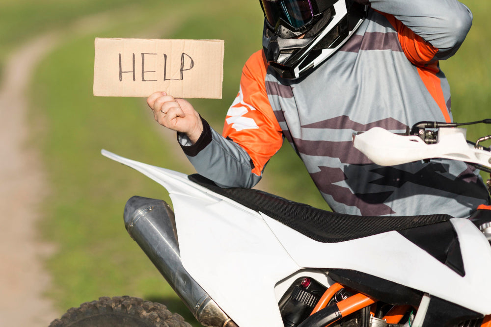 motocyklista przy motorze z kartką proszącą o pomoc