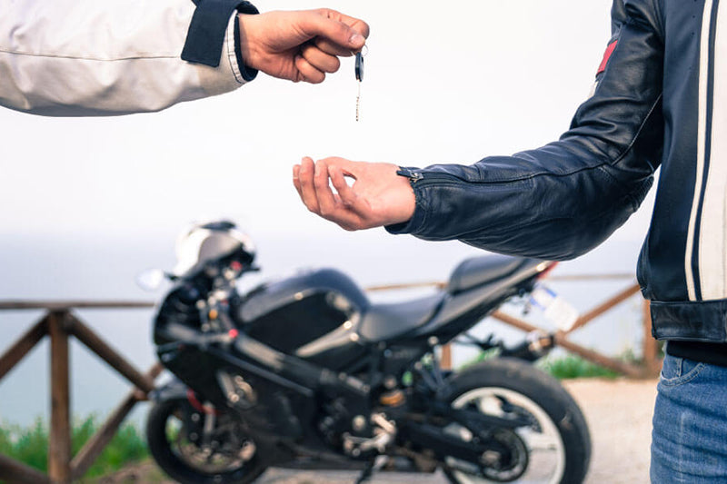 na tle motocyklu dwie osoby przekazują sobie kluczyki