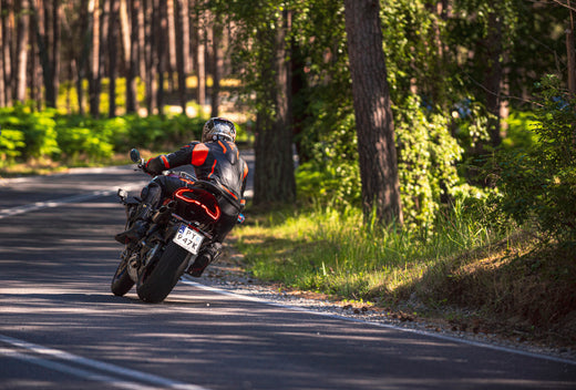 Motocykl w trasie, na pobocznej drodze, motocyklista w kombinezonie i kasku, na poboczu gęste drzewa