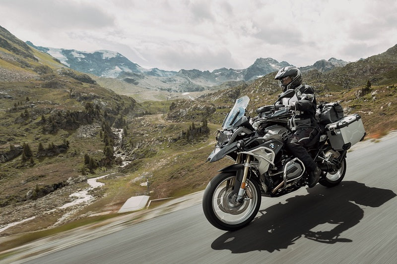 motocyklista na motocyklu BMW z kuframi SW-MOTECH jedzie drogą po terenie górzystym