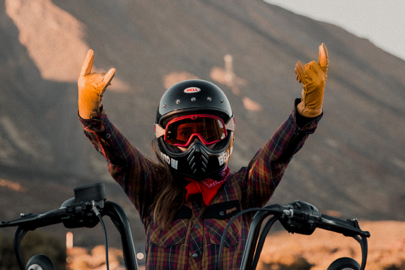 Motocyklistka z koszuli, kasku motocyklowym bell i rękawicach motocyklowych Broger pozująca do zdjęcia z wyciągniętymi rękoma, w tle góy