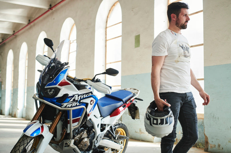 Mężczyzna przy motocyklu trzymający kask. Motocykl w kolorze biało niebieskim z logo Africa