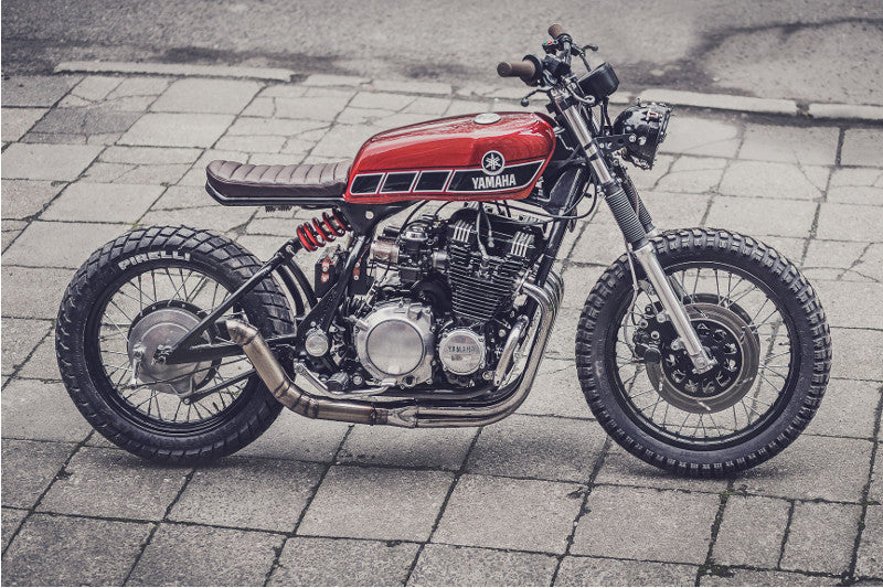 Motocykl customowy czerwony zaparkowany na betonowym chodniku, widoczny bokiem