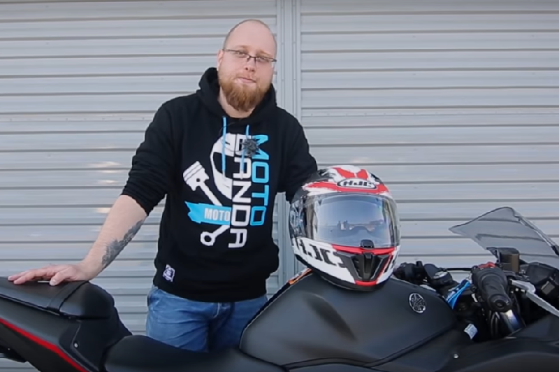 mężczyzna trzyma kask na baku motocykla i się uśmiecha