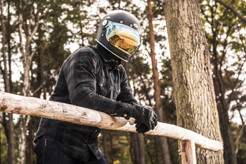 motocyklista w kasku Bell i koszuli Rebelhorn w kolorach czarnych stoi w lesie przy barierce