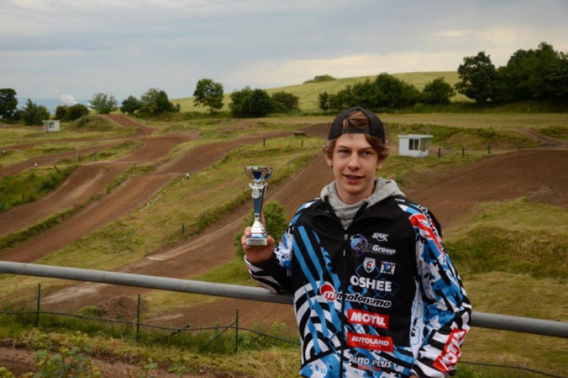 zawodnik trzyma mały puchar, w tle tor motocrossowy