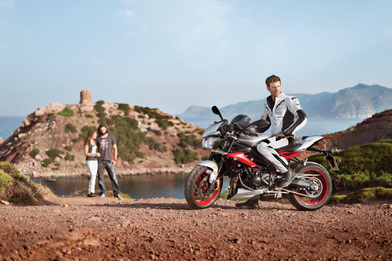 motocyklista stoi przy brzegu, w tle jest wyspa i dwójka turystów