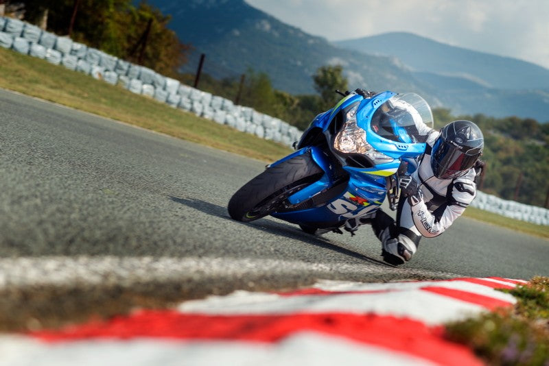 motocyklista na niebieskim motocyklu jedzie po torze, ma ubrany biały sportowy kombinezon Helda