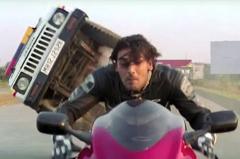 motocyklista na czerwonym motocyklu a za nim samochód, który się wywraca