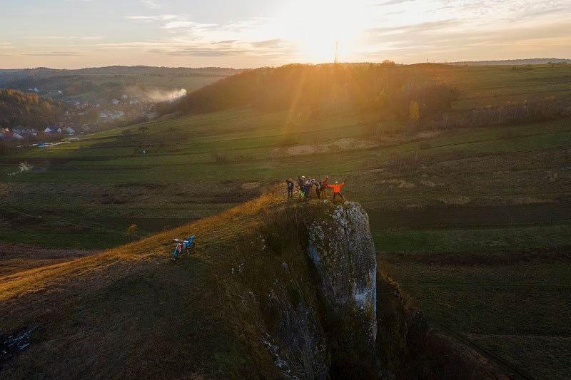 grupa motocyklistów na skale podnosi ręcę obok nich motocykl typu enduro