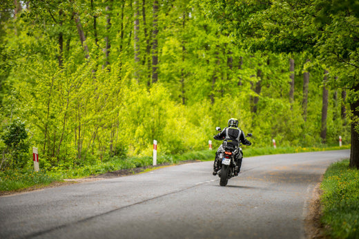 Motocyklista na pobocznej drodze w gęstym lesie, w kasku i kombinezonie motocyklowym