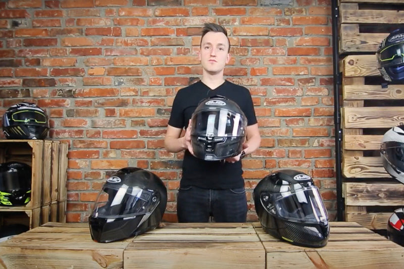 mężczyzna stoi na tle ceglanej ściany, w ręku trzyma kask motocyklowy, na blacie przed nim kaski motocyklowe