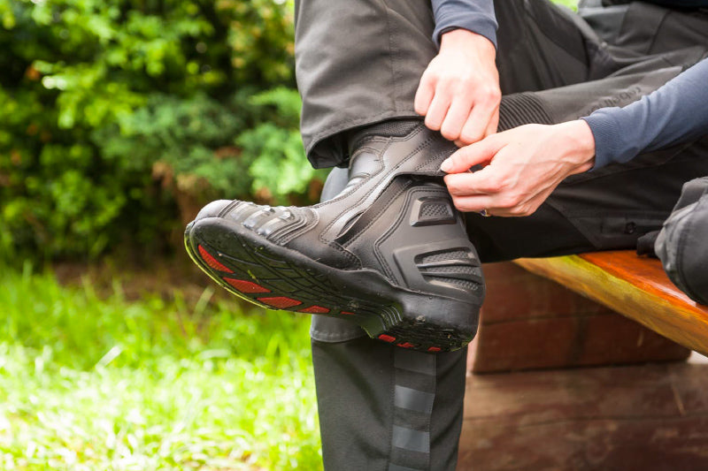 zbliżenie na buty, które właśnie zapina motocyklista siedząc na ławce