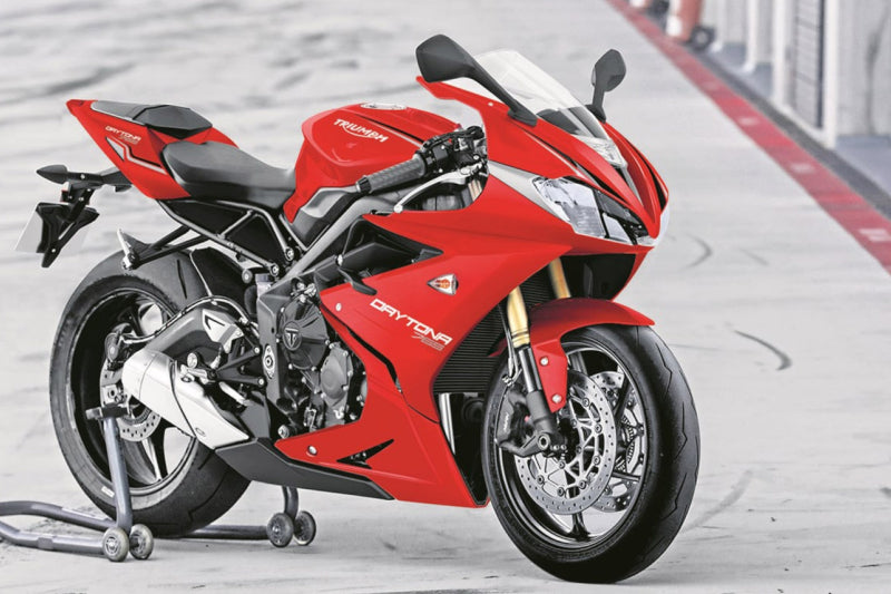 Czerwony motocykl sportowy marki Triumph zaparkowany na podjeździe przed garażami