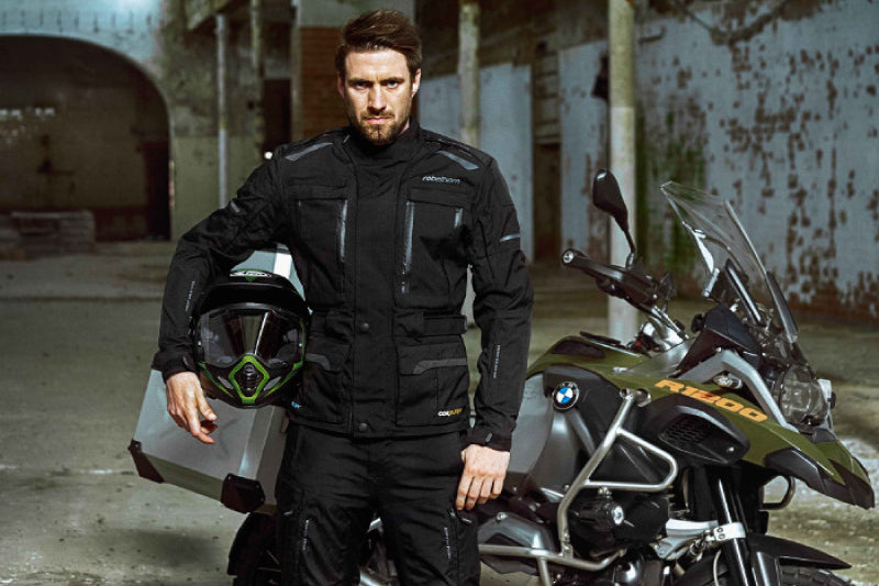 mężczyzna stoi z kaskiem pod pachą przed swoim motocyklem BMW R1200GS w industrialnej przestrzeni