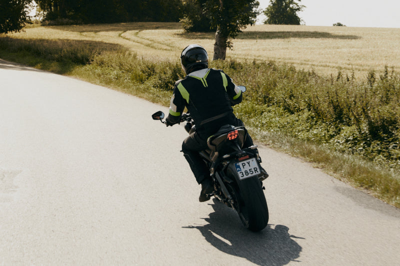 Postać na motocyklu jedzie polną drogą