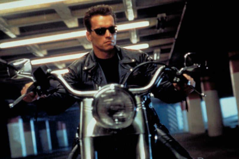 Kadr z filmu terminator z siedzącym na motocyklu Arnoldem Schwarzeneggerem na ciemnym tle w długim korytarzu