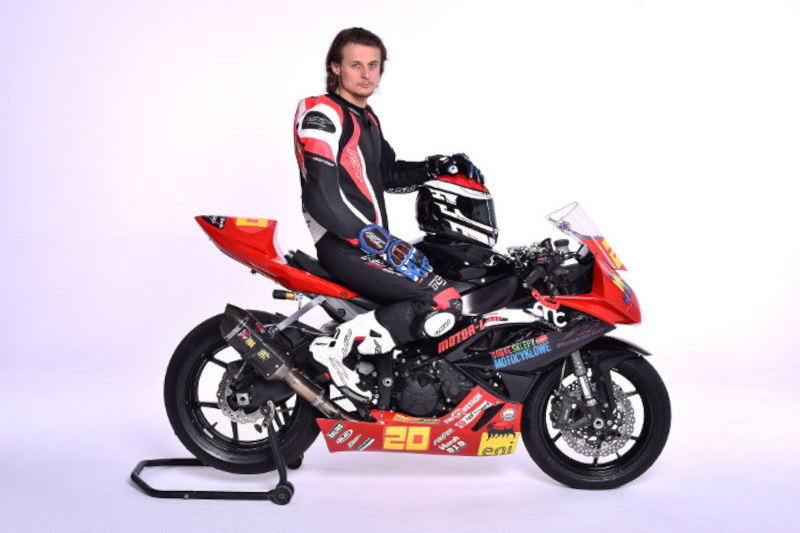 Paweł Rinas pozujący na sportowym motocyklu z kaskiem trzymanym na baku na białym tle