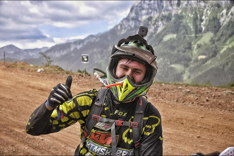 OSKAR KACZMARCZYK podczas zawodów enduro pozujący do zdjęcia z wyciągniętych w górę kciukiem, w tle trasa wyścigu enduro