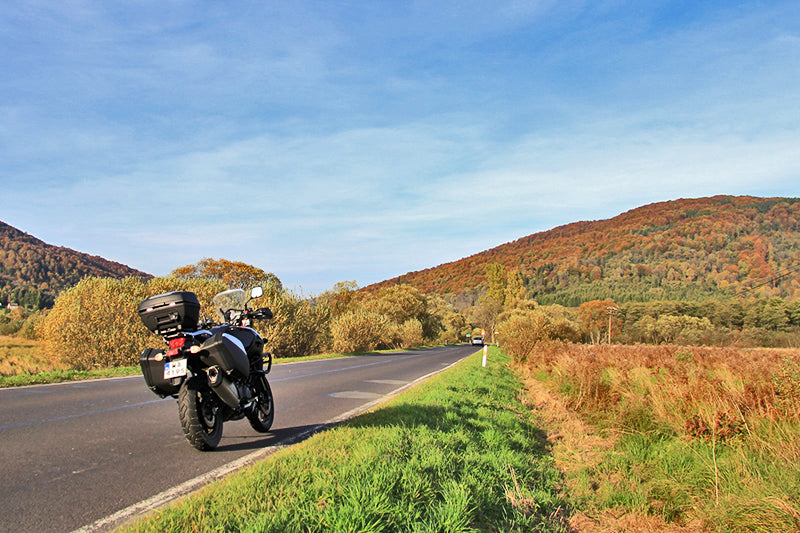 Motocykl turystyczny stojący na poboczu drogi w Bieszczadach, w tle drzewa i pagórki, jasne niebo