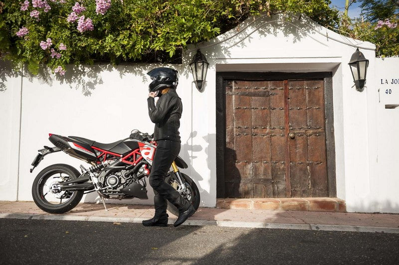 Motocykl zaparkowany przy drzwiach, obok niego podchodzący motocyklista w kasku motocyklowym