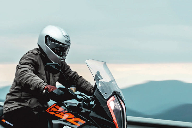 motocyklista jedzie drogą, ma założony jesienny kask motocyklowy, w tle widać góry