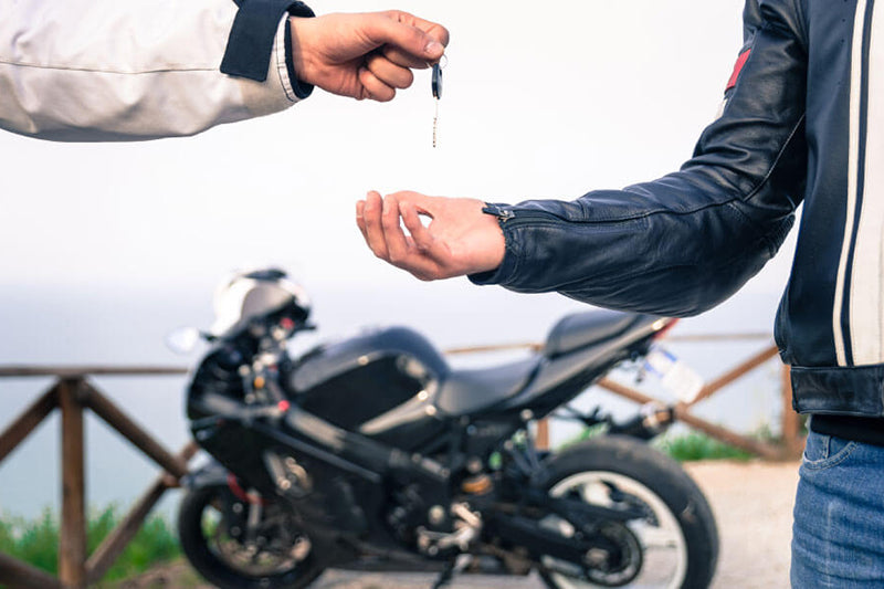 dwóch mężczyzn, jeden przekazuje kluczyki drugiemu, w drugim planie kupowany motocykl