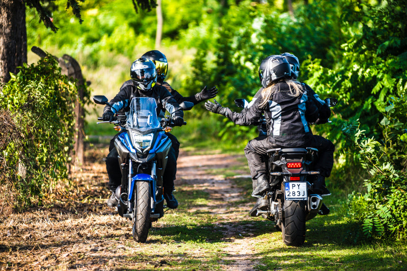 dwoje motocyklistów mijających się na bocznej drodze pozdrawiających się lewą ręką uniesioną do góry