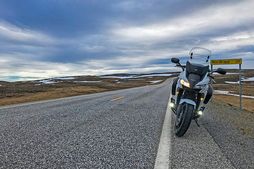 Motocykl turystyczny zaparkowany na poboczu długiej drogi, w tle zachmurzone niebo i pagórki