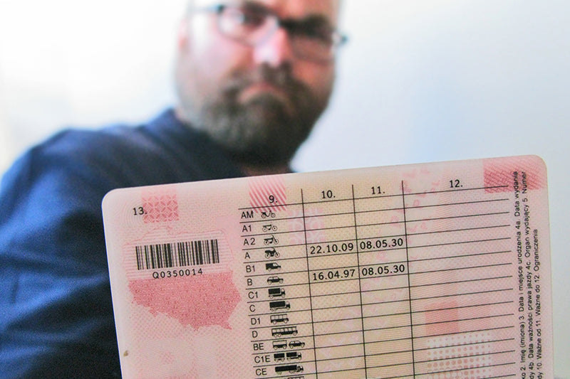Mężczyzna w okularach pokazujący tylną część polskiego dokumentu prawa jazdy w zbliżeniu