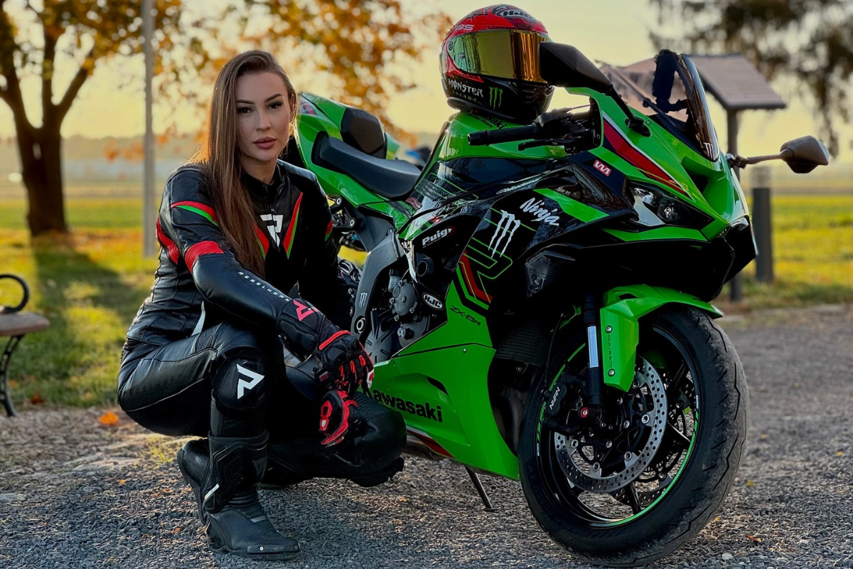 Magdalena Plich z motocyklu Kawasaki Ninja, pozująca na tle jesiennego krajobrazu z drzewami i ciepłym światłem słonecznym.