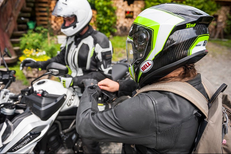 Motocyklista w kasku Bell i kurtce skórzanej motocyklowej poprawiający rękawicę motocyklową, obok niego drugi motocyklista siedzący na motocyklu w kasku motocyklowej z podniesioną blendą