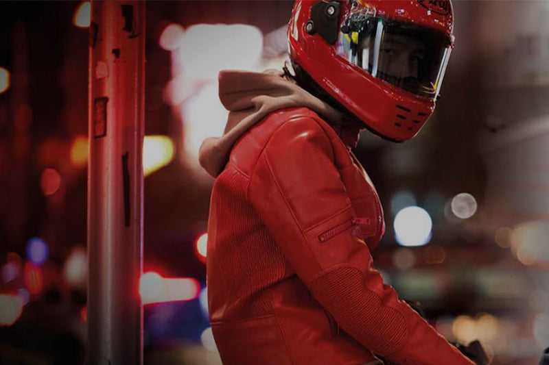 motocyklista w czerwonej kurtce skórzanej i czerwonym kasku siedzi bokiem na motocyklu