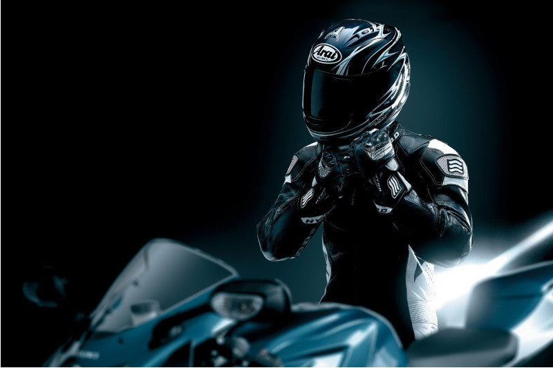 czarne zdjęcie: na czarnym tle widać siedzącego na czarnym motocyklu motocyklistę ubranego w czarny kask motocyklowy Arai