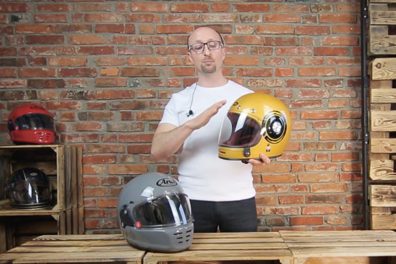 Mężczyzna prezentujący dwa kaski motocyklowej marek Arai Concept X czy Bell Bullitt. Kaski w kolorach szarym i żółtym