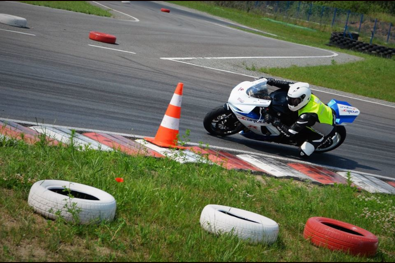 Motocyklista w kasku motocyklowym i kamizelce odblaskowej jadący po torze motocyklowym obok słupka