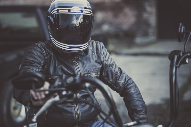 Motocyklista w kasku Bell oraz skórzanej kurtce na czarnym motocyklu