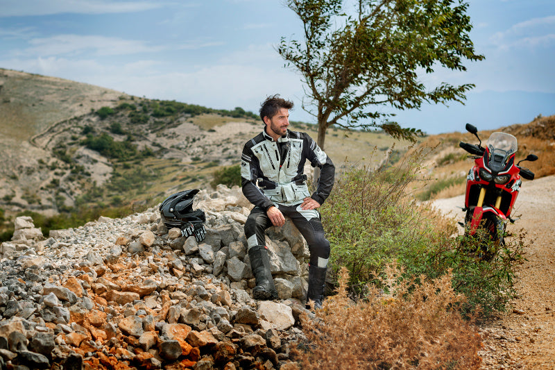 mężczyzna siedzi na skale obok swojego motocykla w turystycznym ubraniu motocyklowym