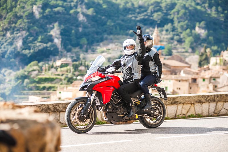 Para motocyklistów w kaskach na czerwonym sportowym motocyklu w turystycznym mieście, kierowca pozdrawia wyciągniętą dłonią