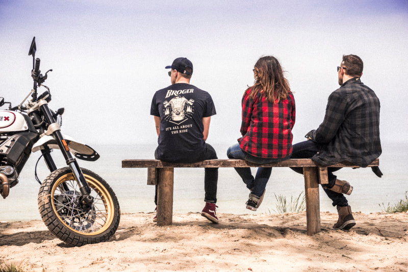 troje motocyklistów siedzących tyłem na ławce, latem, ubrani w ciuchy motocyklowe od Brogera