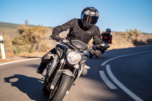 Motocyklista na motocyklu w kasku Bell i kurtce motocyklowej Rebelhorn, wchodzący w zakręt, za nim drugi motocyklista