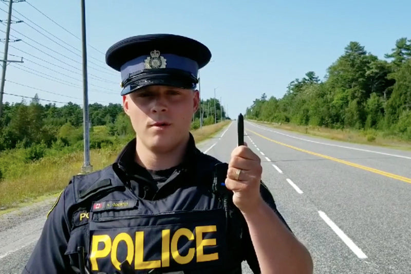 Kadr w filmu motocykl za długopisem. Policjant z żółtym napisem Police, stojący na drodze z podniesioną ręką i długopisem. 