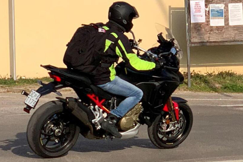 Motocyklista na czarno-czerwonym motocyklu w kurtce motocyklowej i kasku, z plecakiem
