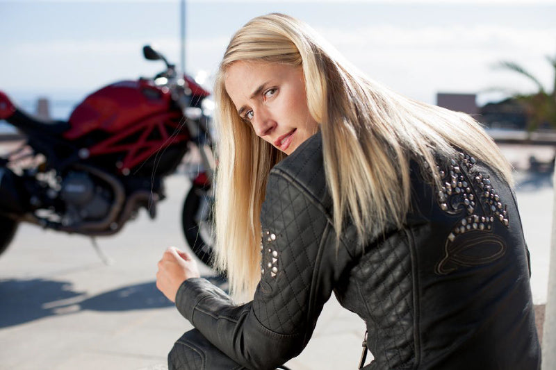 kobieta w skórzanej kurtce motocyklowej siedząca w słoneczny dzień na tle motocykla Ducati