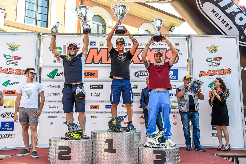 Podium ze zwycięzcami zawodów Enduro IC, podnoszącymi do góry swoje puchary