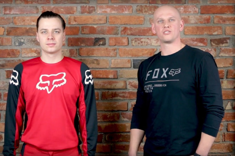 Kadr z filmu, dwóch mężczyzn w ubraniach foxa, model foxa i osoba opisująca strój na motocross
