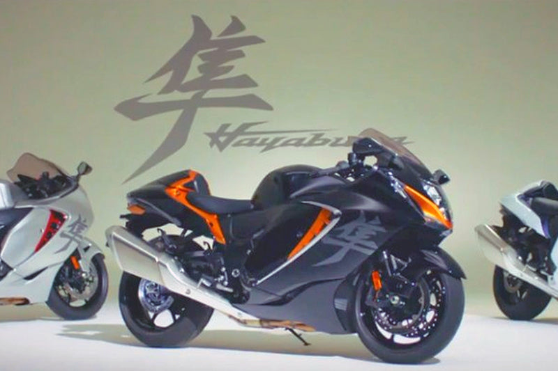 Motocykl Suzuki Hayabusa prezentowany w kolorystyce czarno-pomarańczowej. Sportowy motocykl obok innych widocznych motocykli hayabusa.