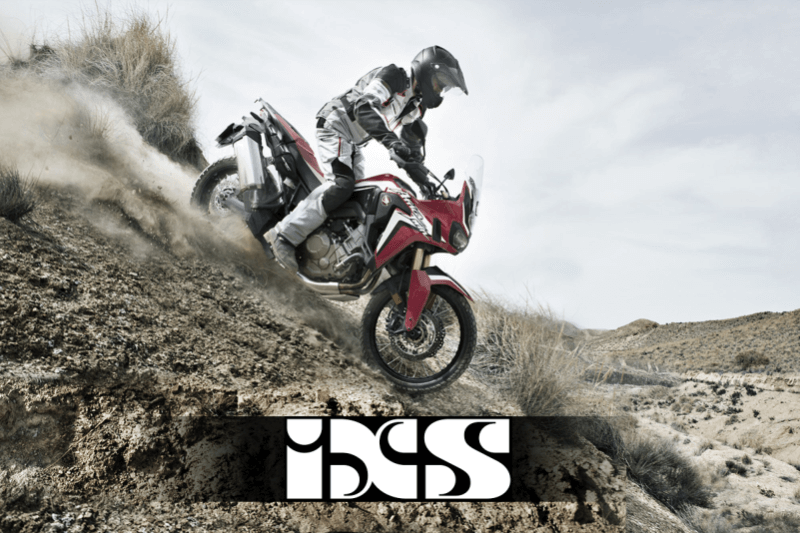 Motocyklista zjeżdżający ze skarpy na motocyklu, w kombinezonie motocyklowym i kasku, zdjęcie z logo ixs