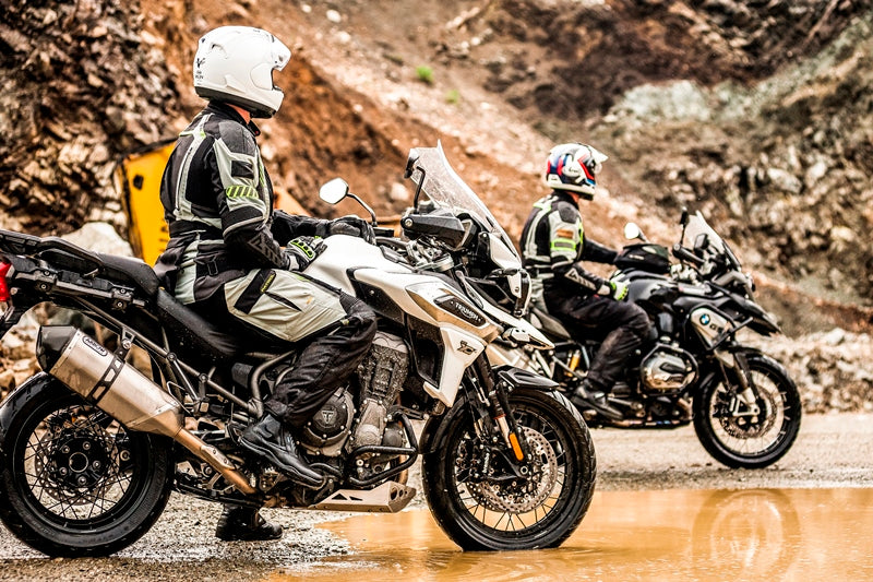 Dwóch motocyklistów w czasie offroadowej wyprawy motocyklowej, stoją na motocyklach pośrodku błota i skał. Mają na sobie kombinezony rebelhorn patrol i buty motocyklowe rebelhorn