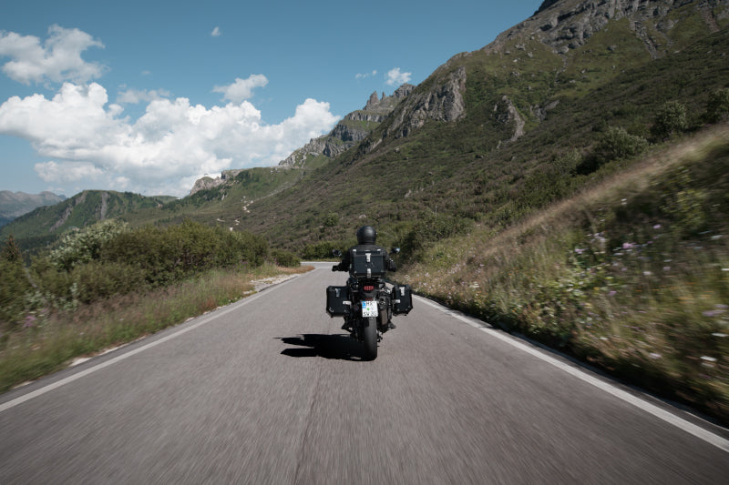 motocyklista jadący górską drogą na motocyklu adventure, z boku ma kufry motocyklowe sw motech